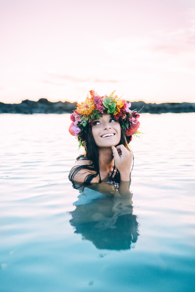 Family Photographer, a beautiful young woman stands in the water, she smiles and wears a colorful floral crown.